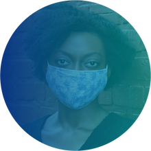 Image of black woman with short, curly, natural hair wearing a face mask and standing in front of a brick wall